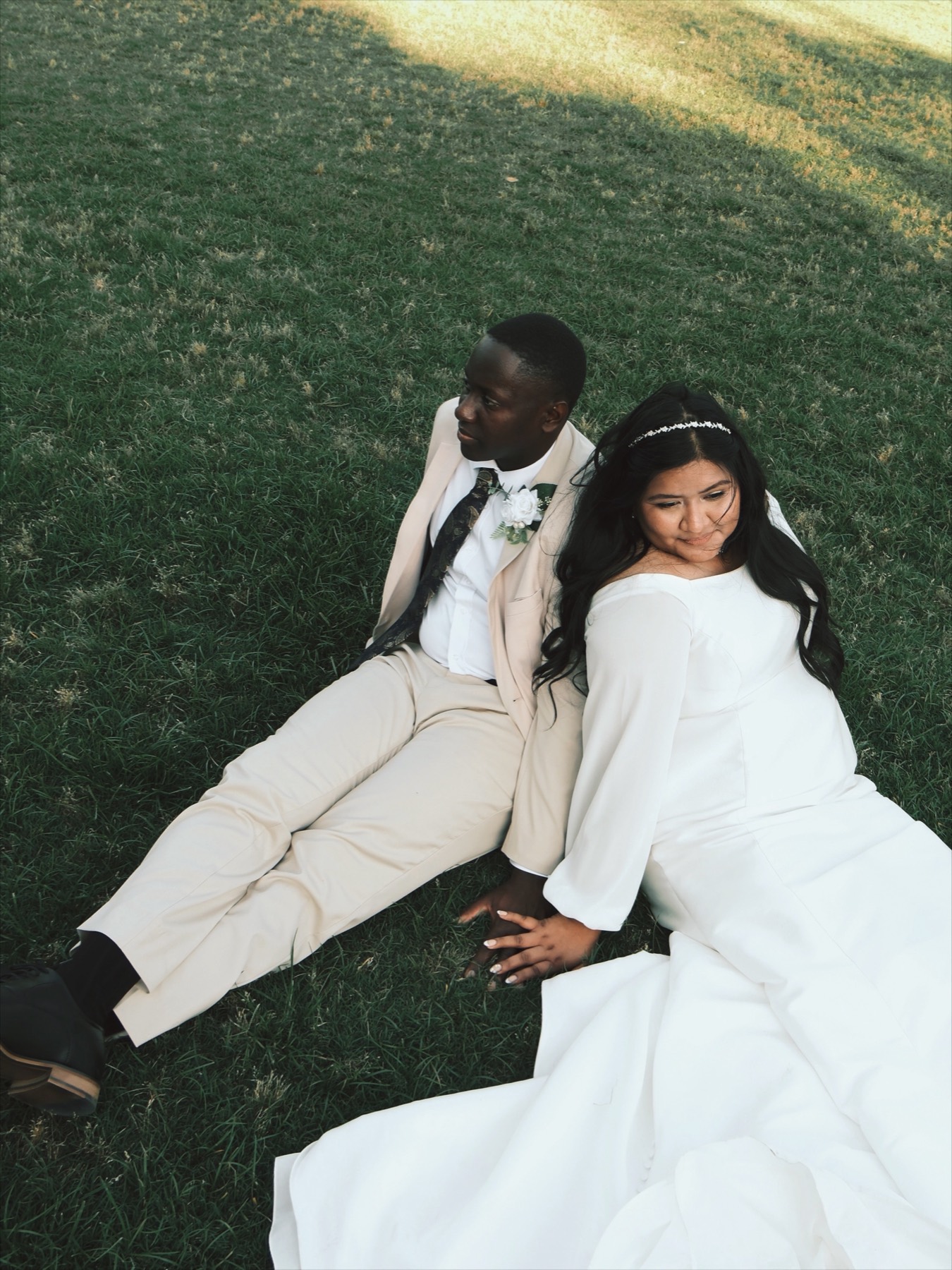 Bride and groom sitting back-to-back on grass